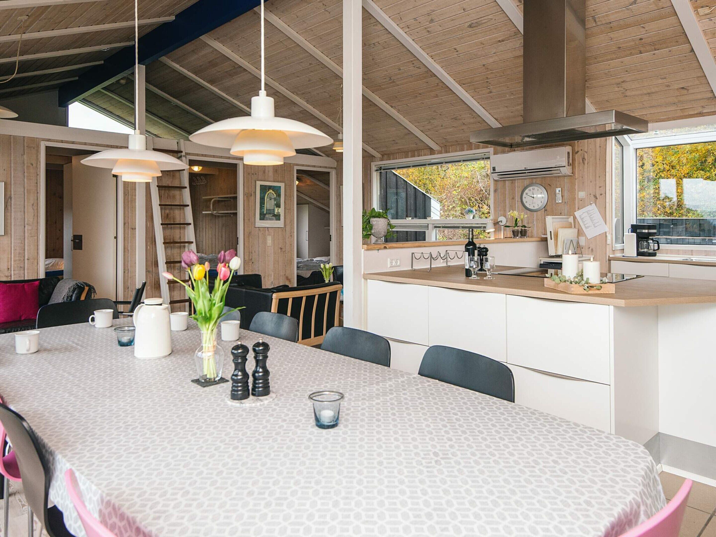 Una cocina moderna con una isla grande, techo de madera y vistas a árboles otoñales a través del ventanal.