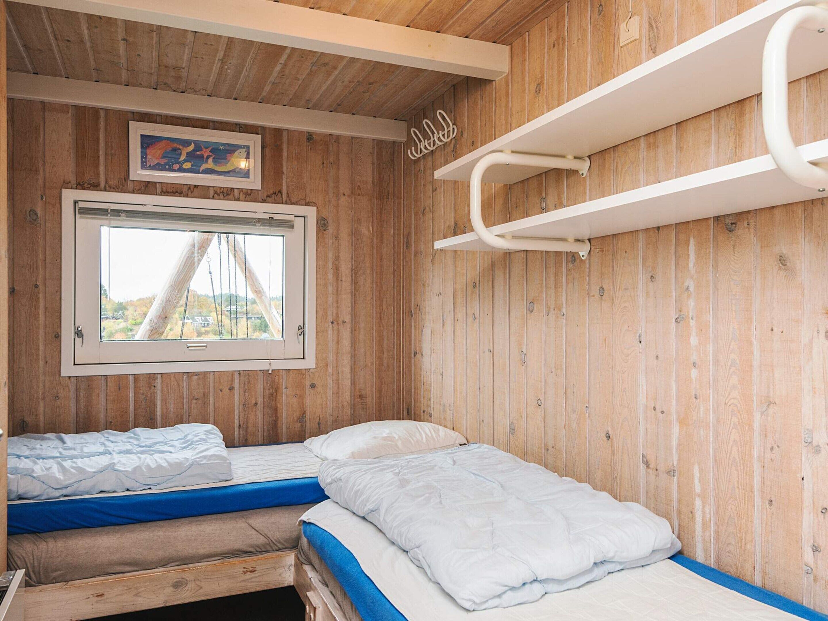 Una habitación de cabaña de madera con dos camas, una ventana con vistas y un estante blanco.