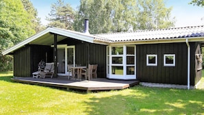 Eine Holzhütte mit überdachter Veranda, Schornstein und einer kleinen Terrasse.