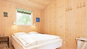 Ein Zimmer mit Holzboden, einem Bett, einem Fenster und einem an der Wand befestigten Kleiderhaken.