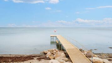 A wooden pier extending into calm waters, surrounded by rocks and pebbles.