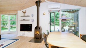 Ein gemütliches Zimmer mit Holzboden, Kamin, Esstisch und Blick auf grüne Natur.