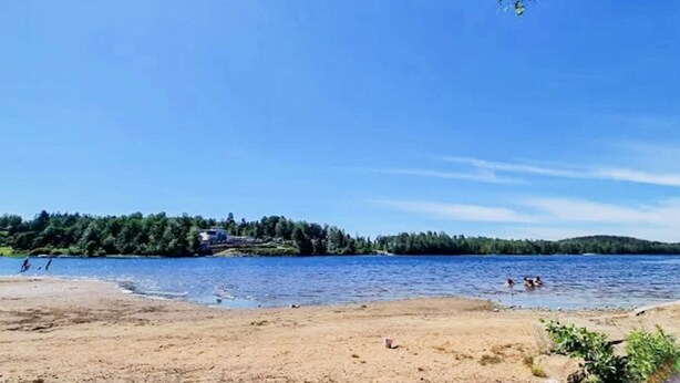 A beach with a clear sky, calm water, and a forested shoreline. - 4 Person Holiday Home in Boras (Borås)