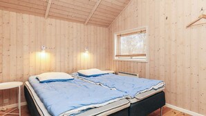 A bedroom with wooden walls, a window, two bedside tables, and a bed with blue bedding.