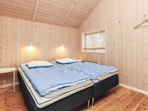 A bedroom with wooden walls, a window, two bedside tables, and a bed with blue bedding. - 5 Star Holiday Home in Hojby (Hojby)