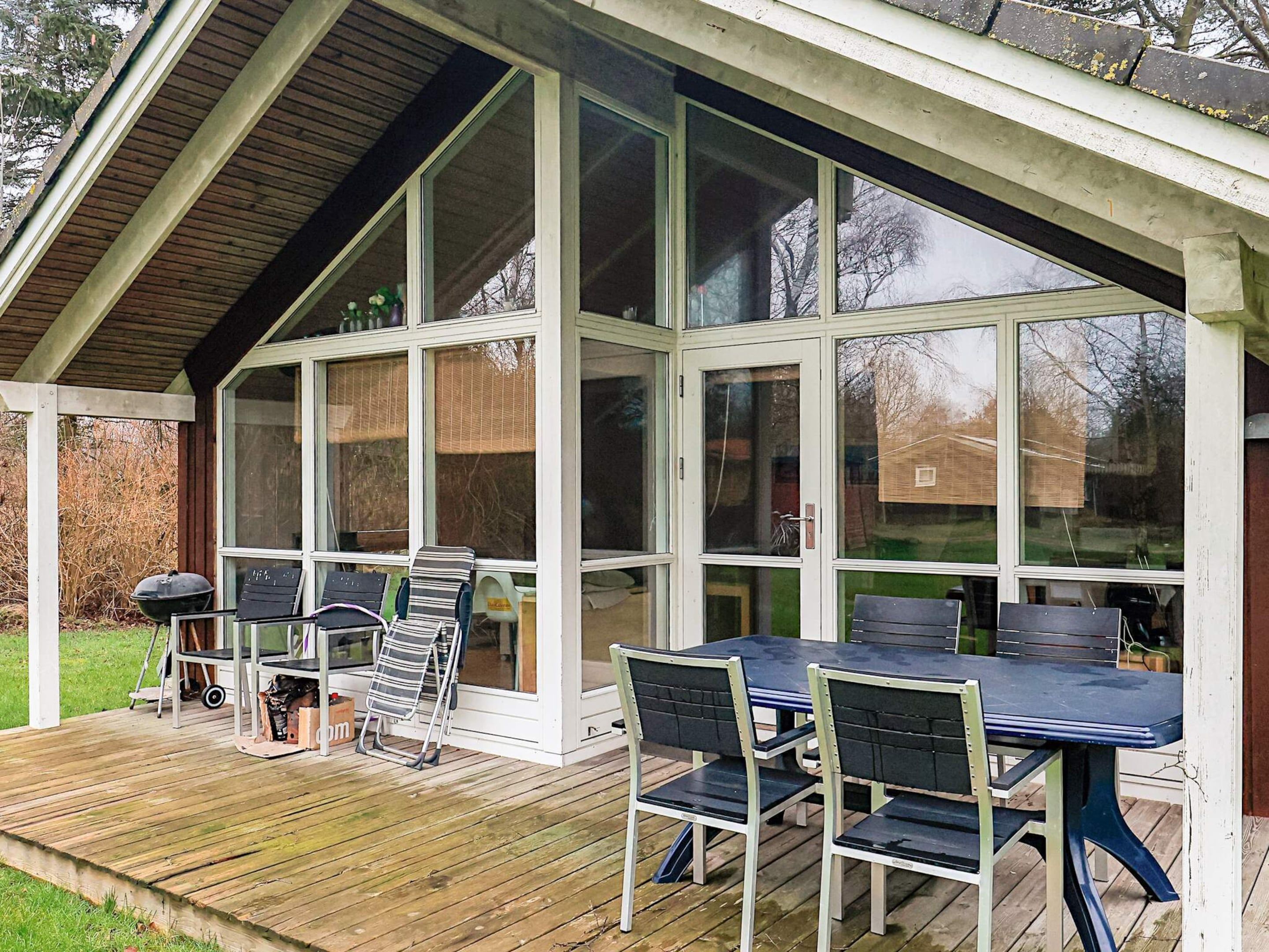 A covered outdoor area with a table and chairs, a grill, and a wooden deck.