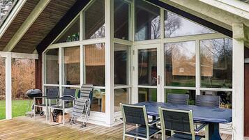 A covered outdoor area with a table and chairs, a grill, and a wooden deck.