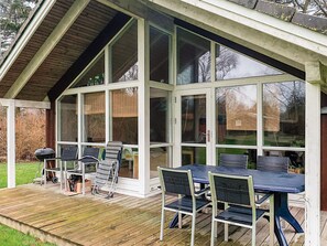 Un espace extérieur abrité, équipé d’une table et de chaises, d’un barbecue et d’une terrasse en bois.