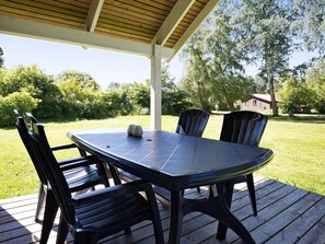 Un espace extérieur abrité, aménagé pour les repas, avec une table et des chaises, entouré d’une terrasse en bois et de verdure.