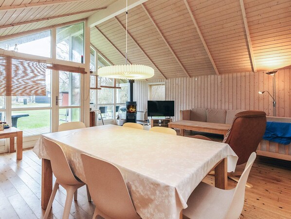 Une pièce chaleureuse avec un décor intérieur en bois, une table à manger avec des chaises, un canapé, un téléviseur et une cheminée.