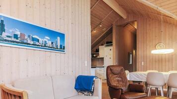 A cozy interior with a wooden ceiling, a cityscape wall art, a sofa, a dining table with chairs, and a kitchen area.