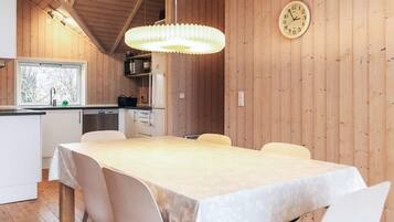 En inredning med träpanel, ett matbord, stolar, en hängande lampa och en väggklocka.
