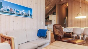A cozy room with a wooden ceiling, a cityscape painting, a sofa, a leather chair, and a dining table with chairs.