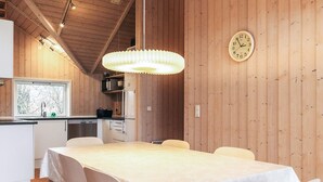 A wooden interior with a dining table, chairs, a hanging light fixture, and a wall clock.
