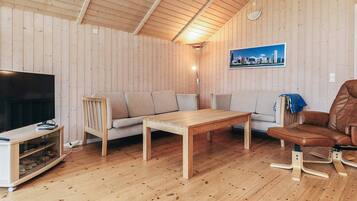 A wooden-paneled room with a television, sofa, table, and a chair.