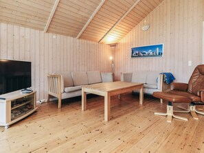 Une pièce aux murs lambrissés, comprenant un téléviseur, un canapé, une table et une chaise.