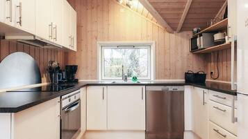 Cozinha moderna com paredes de madeira, uma janela, eletrodomésticos de aço inoxidável e bancada preta.