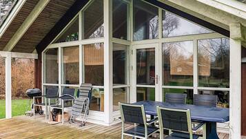 A covered outdoor area with a table and chairs, a grill, and a wooden deck.