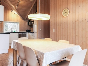 Un intérieur en bois comprenant une table à manger, des chaises, un luminaire suspendu et une horloge murale.