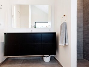 Un baño moderno con un espejo grande, un tocador negro y una toalla colgada en un perchero.