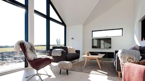 Een moderne woonkamer met een groot raam, een bank, een fauteuil, een salontafel en een flatscreen televisie.