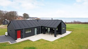 Een modern gebouw met een zwarte gevel, een rode deur en grote ramen.
