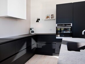A modern kitchen with black cabinetry, a built-in oven, and a coffee machine.