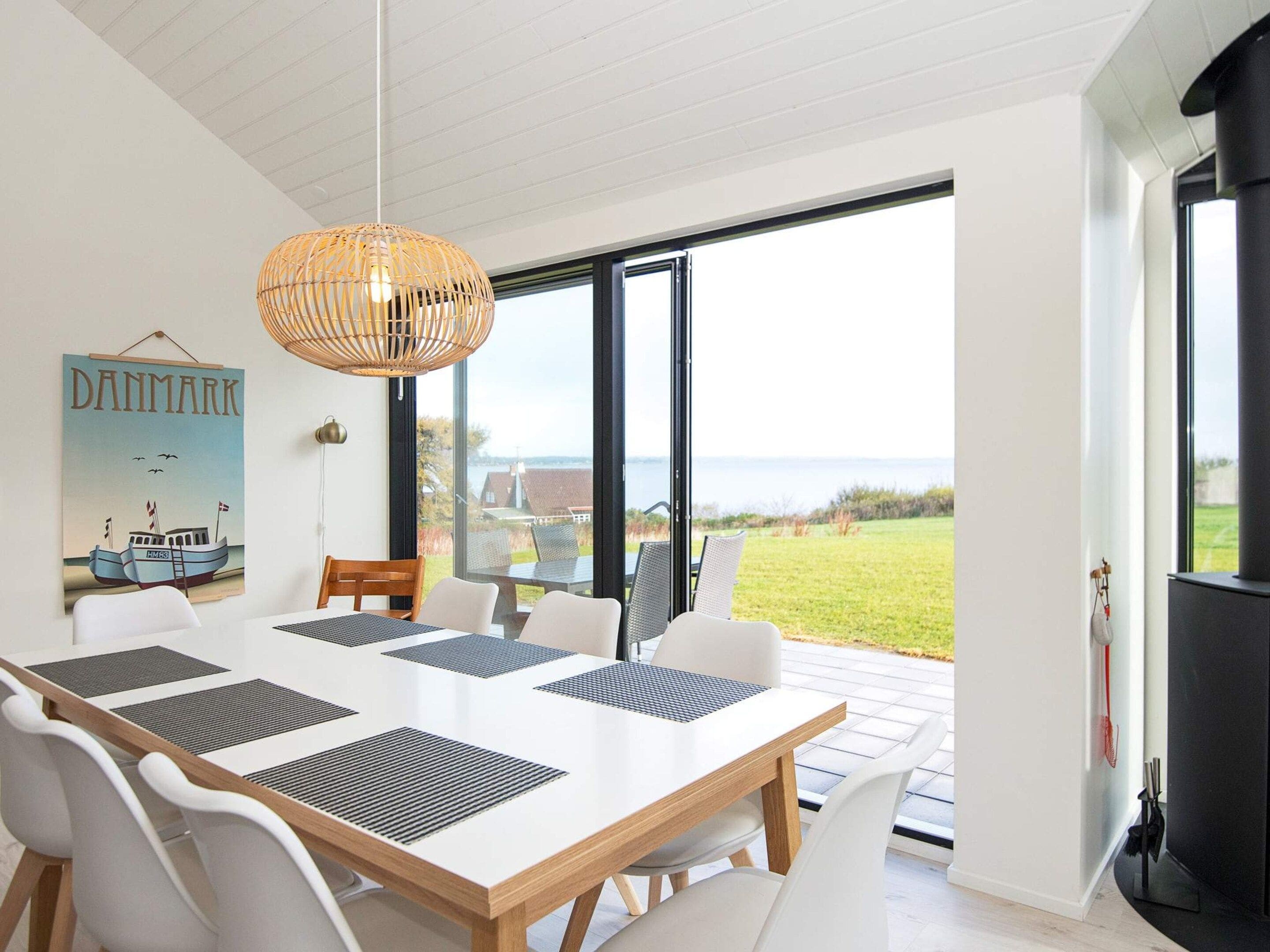 A modern dining area with a large table, white chairs, and a hanging light fixture.