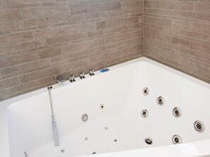 Una bañera blanca con múltiples orificios de desagüe, un cabezal de ducha manual y un grifo.