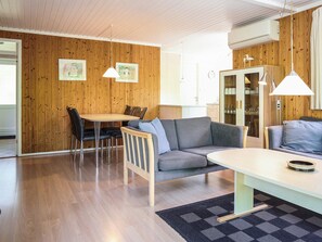 A modern interior with a wooden wall, a dining area with a table and chairs, a sofa, and a kitchen area with cabinets and a refrigerator. - 6 Person Holiday Home in Aakirkeby (Akirkeby)