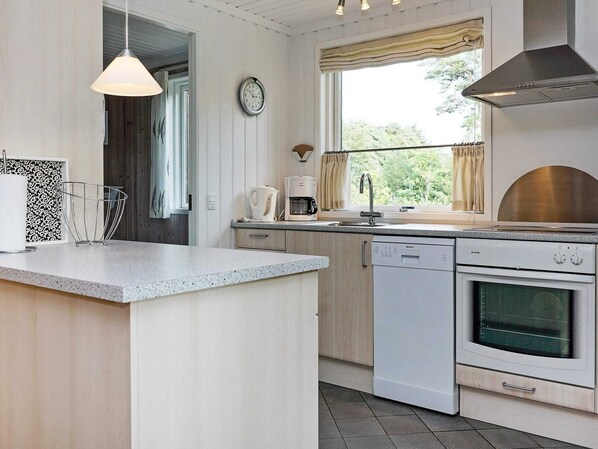 A compact kitchen with a dishwasher, oven, and a window with curtains. - 6 Person Holiday Home in Aakirkeby (Akirkeby)