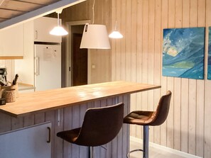 A kitchen with a wooden countertop, two bar stools, pendant lights, and a painting on the wall.