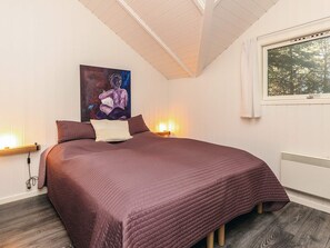A bedroom with a large bed, a painting on the wall, and a window with a view of trees.