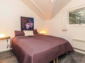 A bedroom with a large bed, a painting on the wall, a window with curtains, and a bedside lamp.