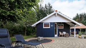 A small, dark blue building with the number 51, a paved patio area with lounge chairs, and a covered seating area with a table and chairs. - 4 Star Holiday Home in Hals (Hals)