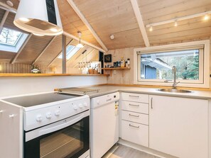 A modern kitchen with a built-in oven, a stovetop, a sink, and a window overlooking a garden. - 4 Star Holiday Home in Hals (Hals)
