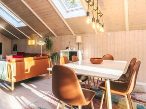 A modern living room with a wooden ceiling, a dining table with chairs, a sofa, and a lamp.