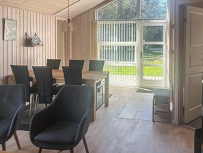 Um quarto com parede revestida de madeira, uma mesa de jantar com cadeiras, um lustre pendurado e um amplo painel de vidro deslizante que dá para uma área externa.