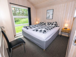 A bedroom with a bed, a chair, a bedside table with a lamp, and a window with a view of greenery. - 6 Person Holiday Home in Hals (Hals)