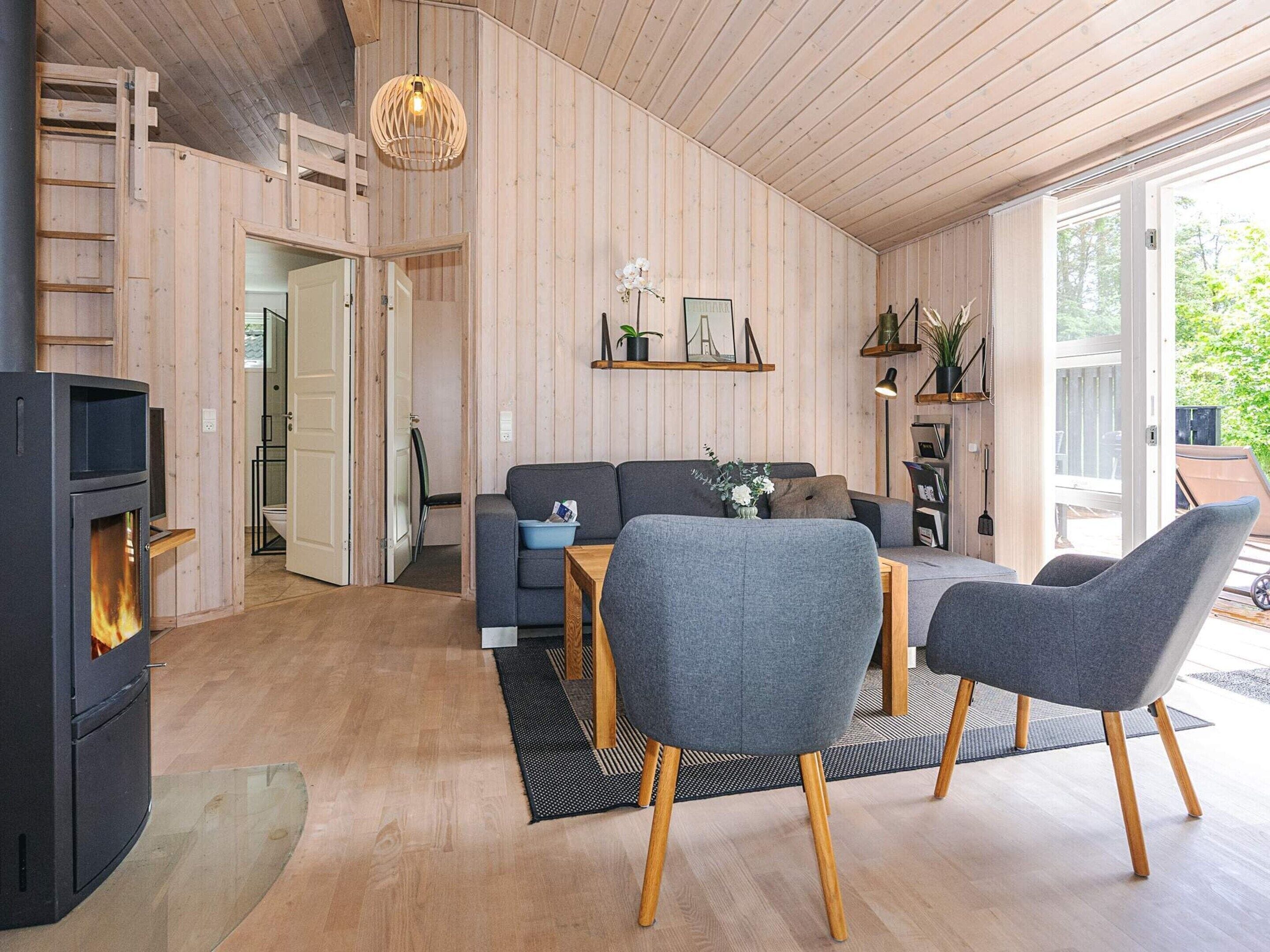 A cozy living room with a fireplace, grey sofas, wooden flooring, and a large window.