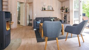 A cozy living room with a fireplace, grey sofas, wooden flooring, and a large window.