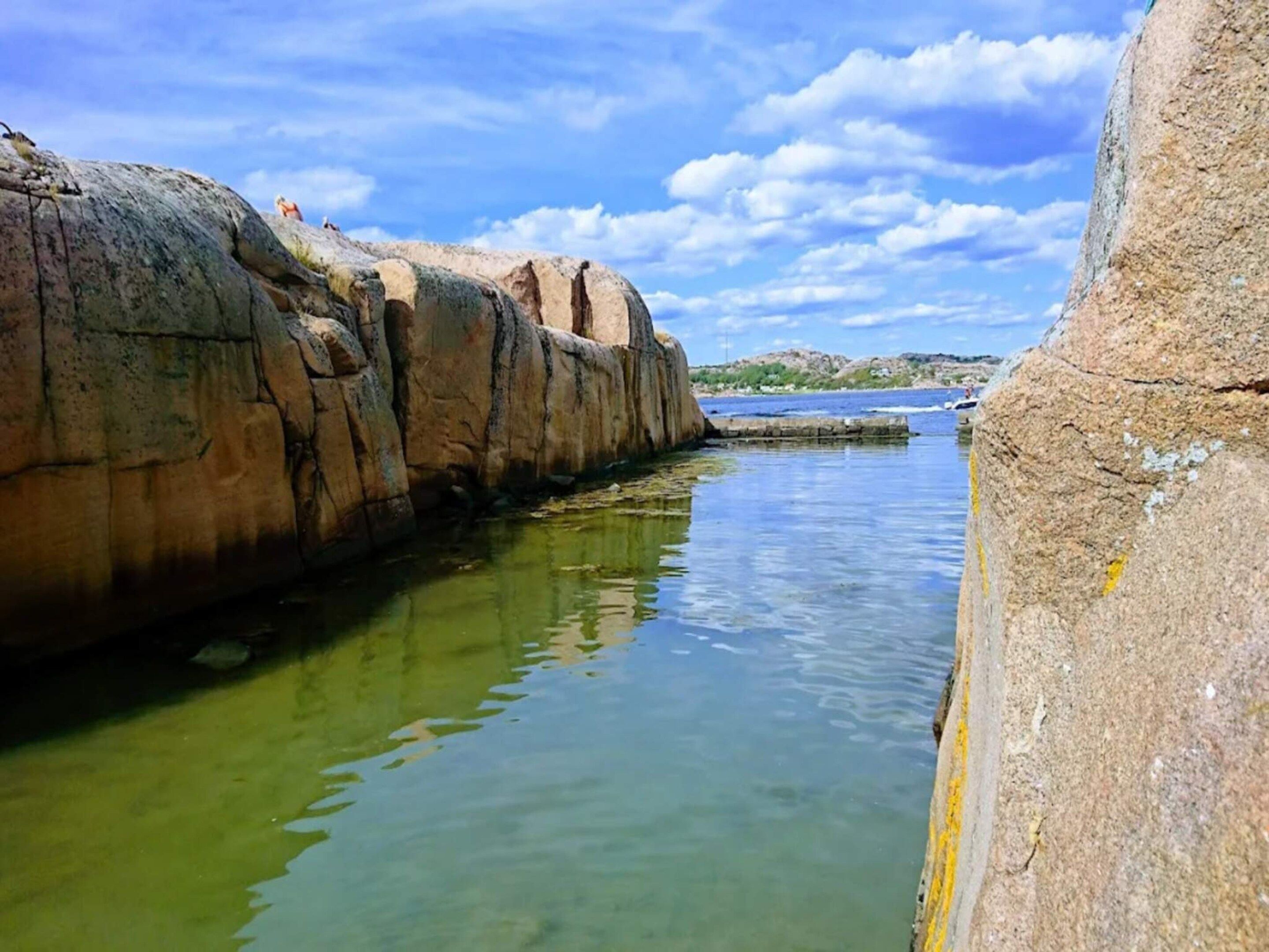A rocky shoreline with clear water and a distant view of land.