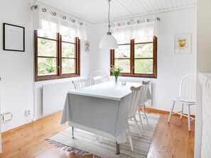 Un coin repas avec une table dressée pour quatre personnes, des chaises blanches, une nappe blanche et un vase rempli de fleurs.