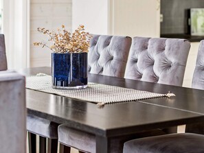 A dining table with a vase of dried flowers, a placemat, and grey upholstered chairs.