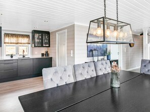 Une cuisine moderne dotée d’un four encastré, d’un coin repas avec une table sombre et des chaises grises à revêtement, et d’un luminaire suspendu.