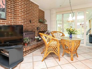 Una sala de estar con chimenea de ladrillo, televisión, sillas de mimbre y una mesa de vidrio.