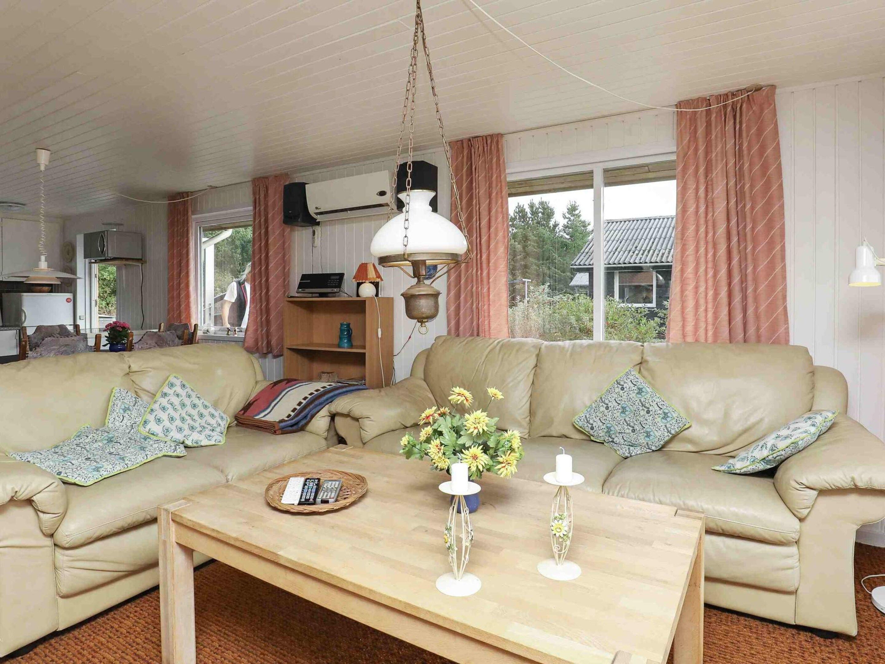Ett vardagsrum med en beige soffa, ett träbord och en hängande lampa.