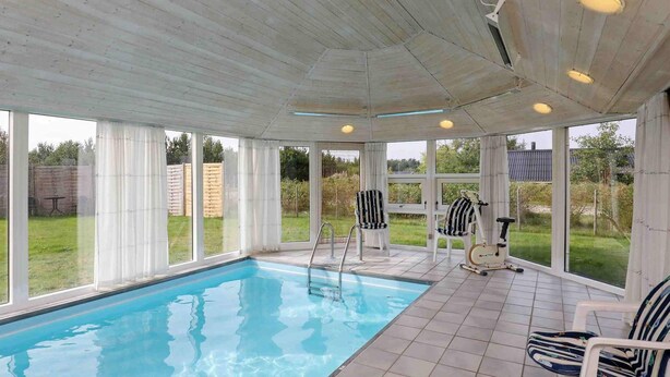 Una piscina techada con piso de baldosas, ventanas amplias y un ventilador de techo.