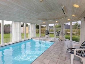 A covered swimming pool with a tiled floor, large windows, and a ceiling fan.
