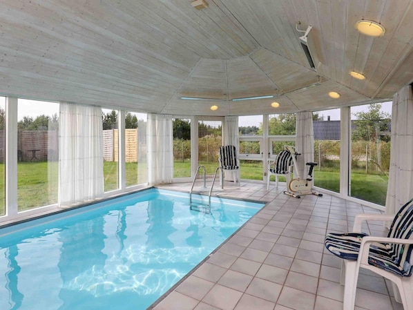Une piscine intĂ©rieure dotĂ©e dâun sol carrelĂ©, de grandes fenĂȘtres et dâun ventilateur de plafond.